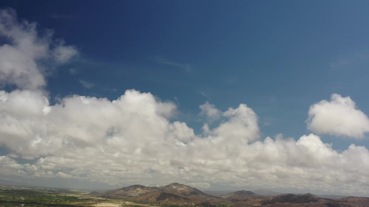 Second frame shows Los Cabos hills stretching across the lower frame while dense white clouds spread through the blue sky, with no visible people.