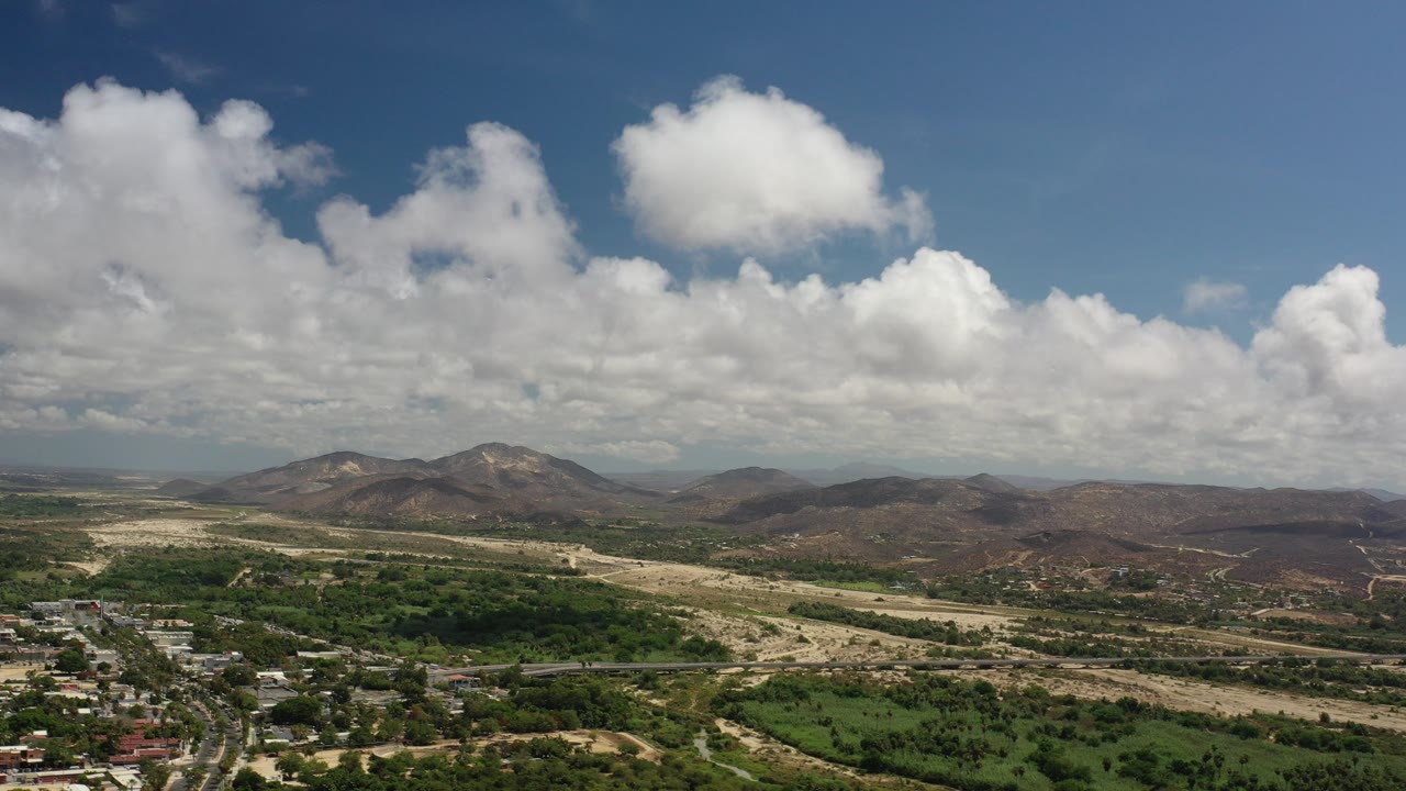 Aerial view of green valley, roads, mountains, and cloudy sky.