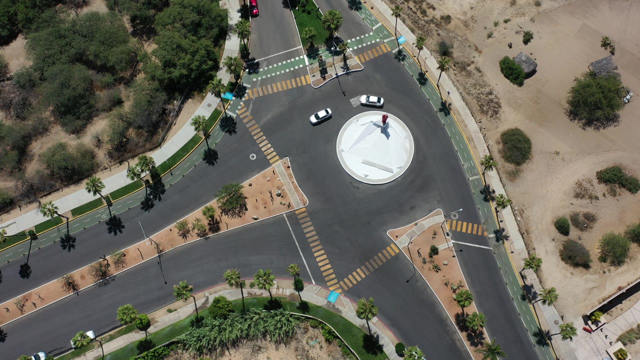 Two white cars curve around a white circular traffic island