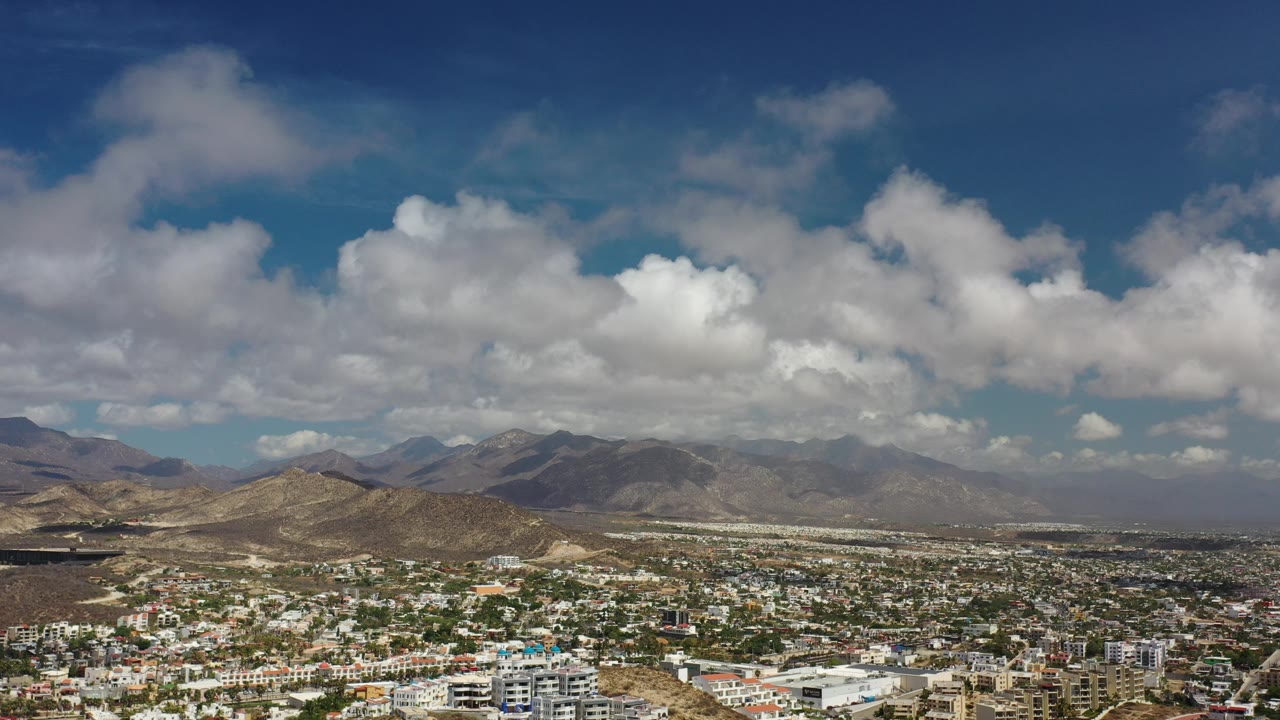 Los Cabos cityscape with layered mountains under thick clouds.