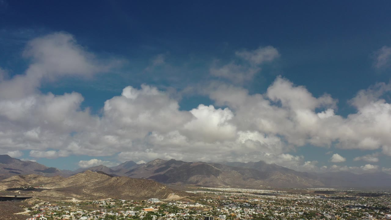 Opening frame of a Los Cabos, Mexico mountain range under a deep blue sky with large white clouds and no visible people.