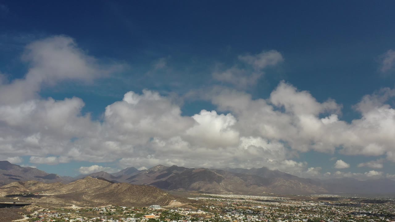 Sunlit hills and distant mountains under a thick line of clouds.