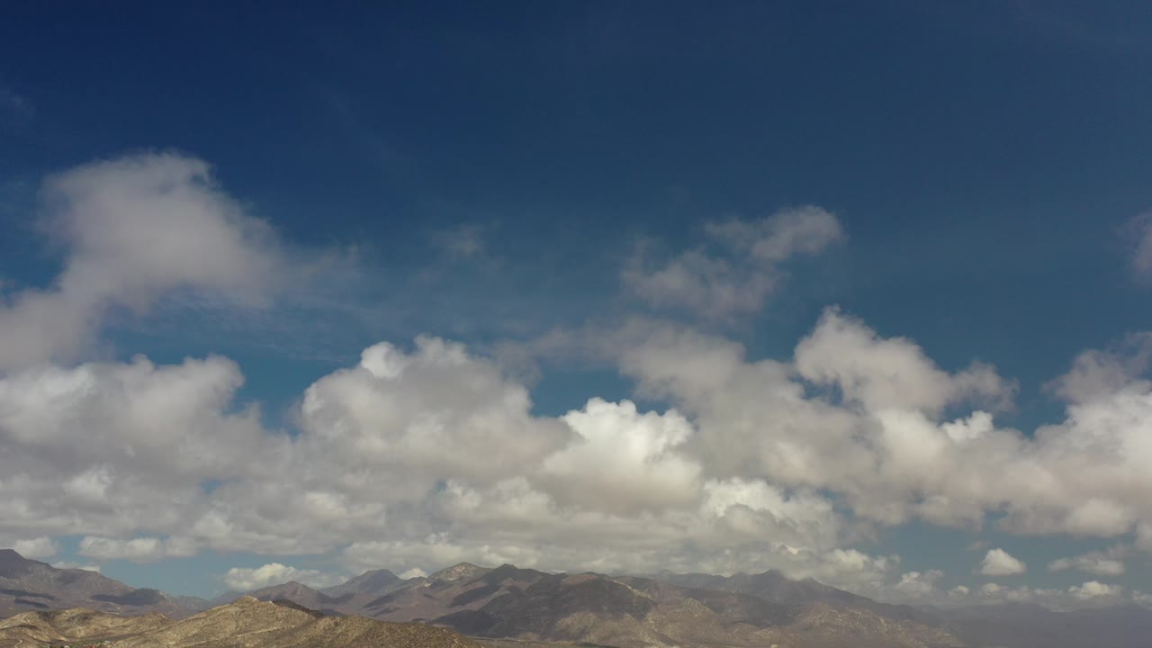 Opening frame of Los Cabos, Mexico showing a low distant mountain range under a deep blue sky with broad white clouds and no visible people.