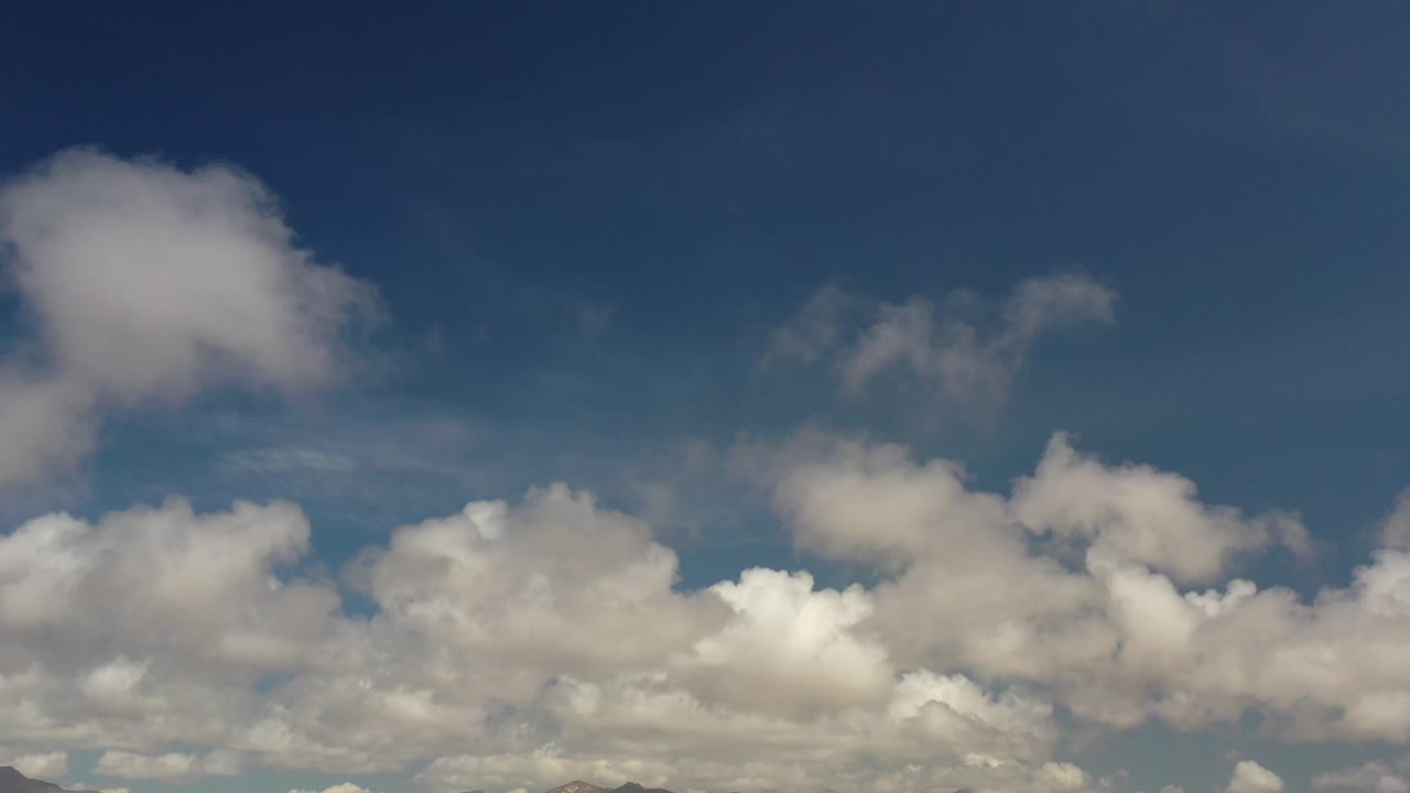Large cumulus clouds hang over a low Los Cabos mountain horizon with only a thin strip of land visible, no visible people.