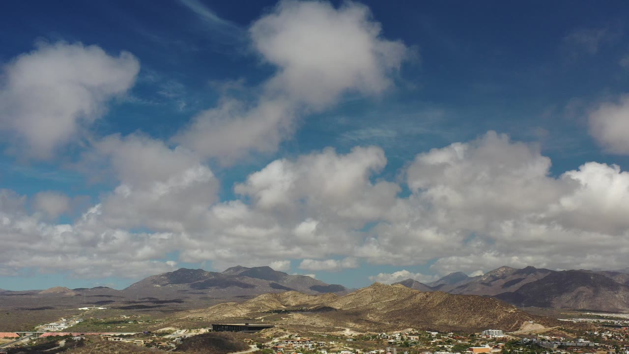 Wide desert mountains beneath a blue sky filled with clouds.