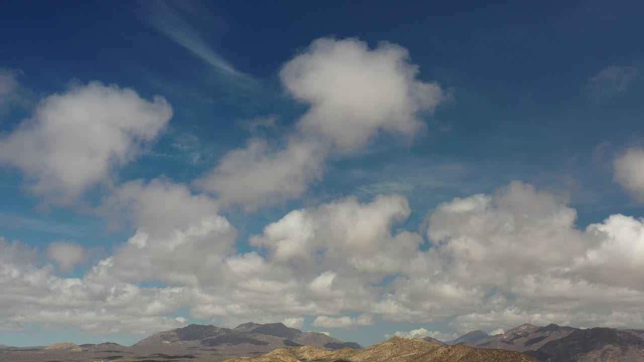 Wide view of puffy white clouds over distant mountains in Los Cabos, Mexico, with no visible people.