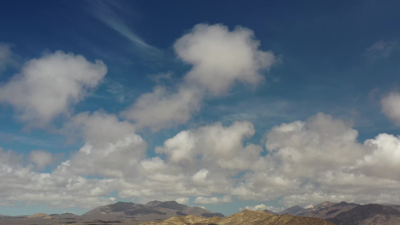 Bright blue sky with large white clouds sitting above a rugged Los Cabos mountain horizon, with no visible people.