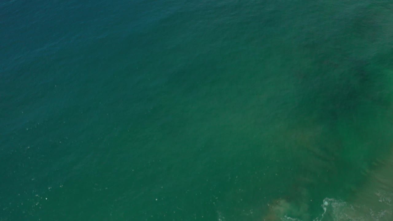 Opening overhead view of blue-green ocean water in Los Cabos, Mexico, with faint darker patches under the surface and no visible people.