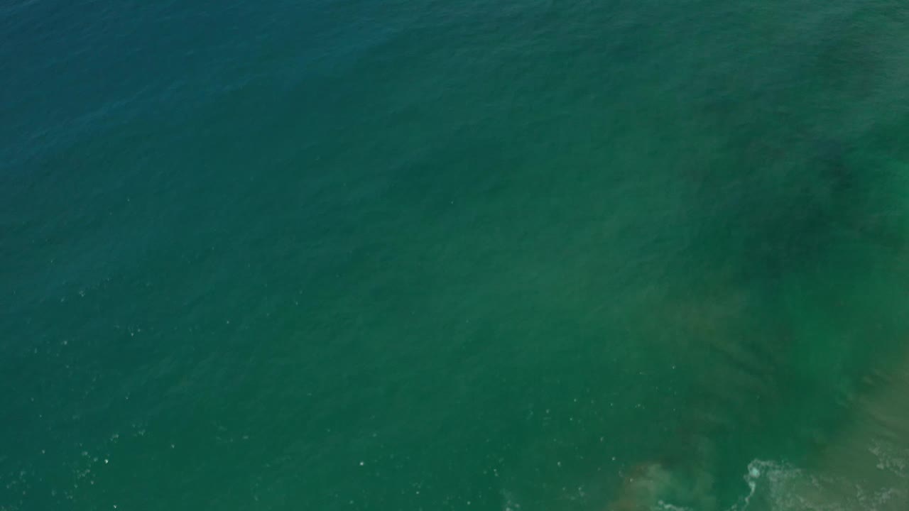 Overhead Los Cabos ocean frame with green water, soft ripple texture, pale underwater haze near the lower edge, and no visible people.