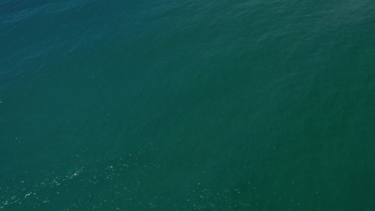 Deep green ocean water in Los Cabos, Mexico fills the first frame with subtle surface ripples, scattered sunlight specks, and no visible people.