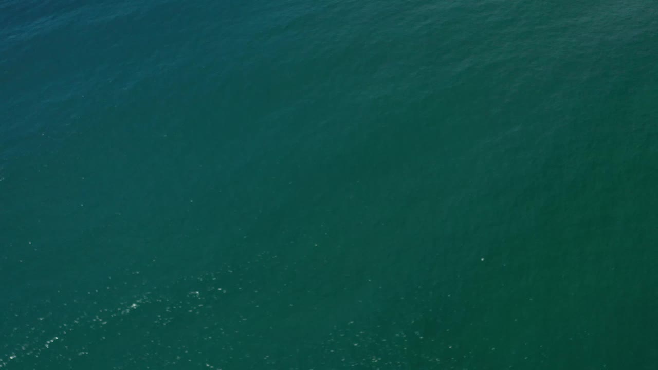 Green sea surface in Los Cabos, Mexico shows a slightly denser line of bright wave sparkle across the lower part of the frame, with no visible people.