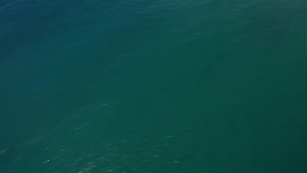Blue-green open sea in Los Cabos, Mexico, with small reflective flecks across the water and no visible people.