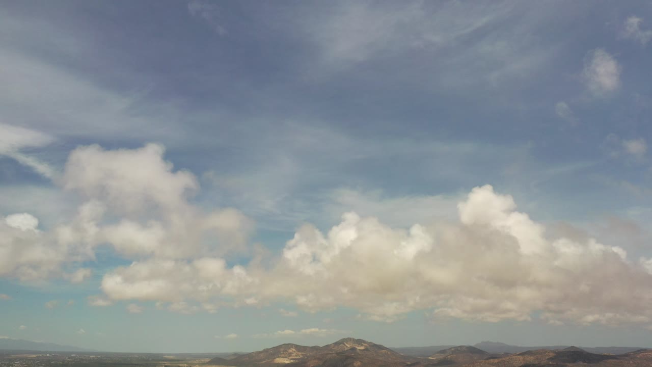Wide aerial valley view under large white clouds