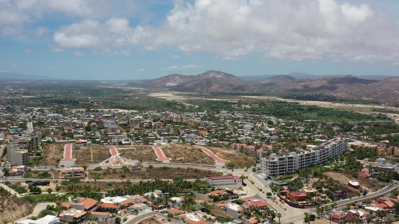 Aerial view of city buildings, roads, dry hills, mountains, and clouds.
