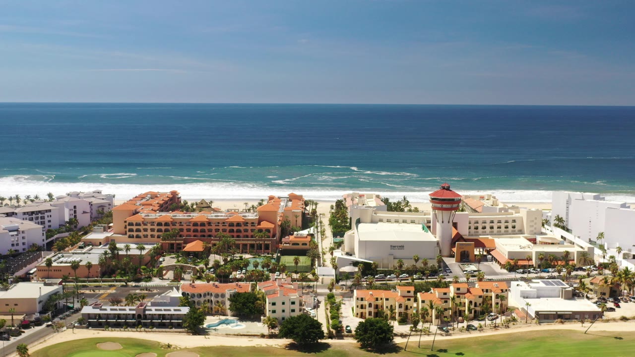 Wide aerial view of ocean, beach surf, and coastal buildings.