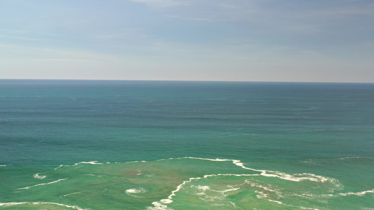 At 0:00, a wide Los Cabos, Mexico ocean view shows turquoise shallows, white surf lines near the bottom edge, hazy sky, and no visible people.