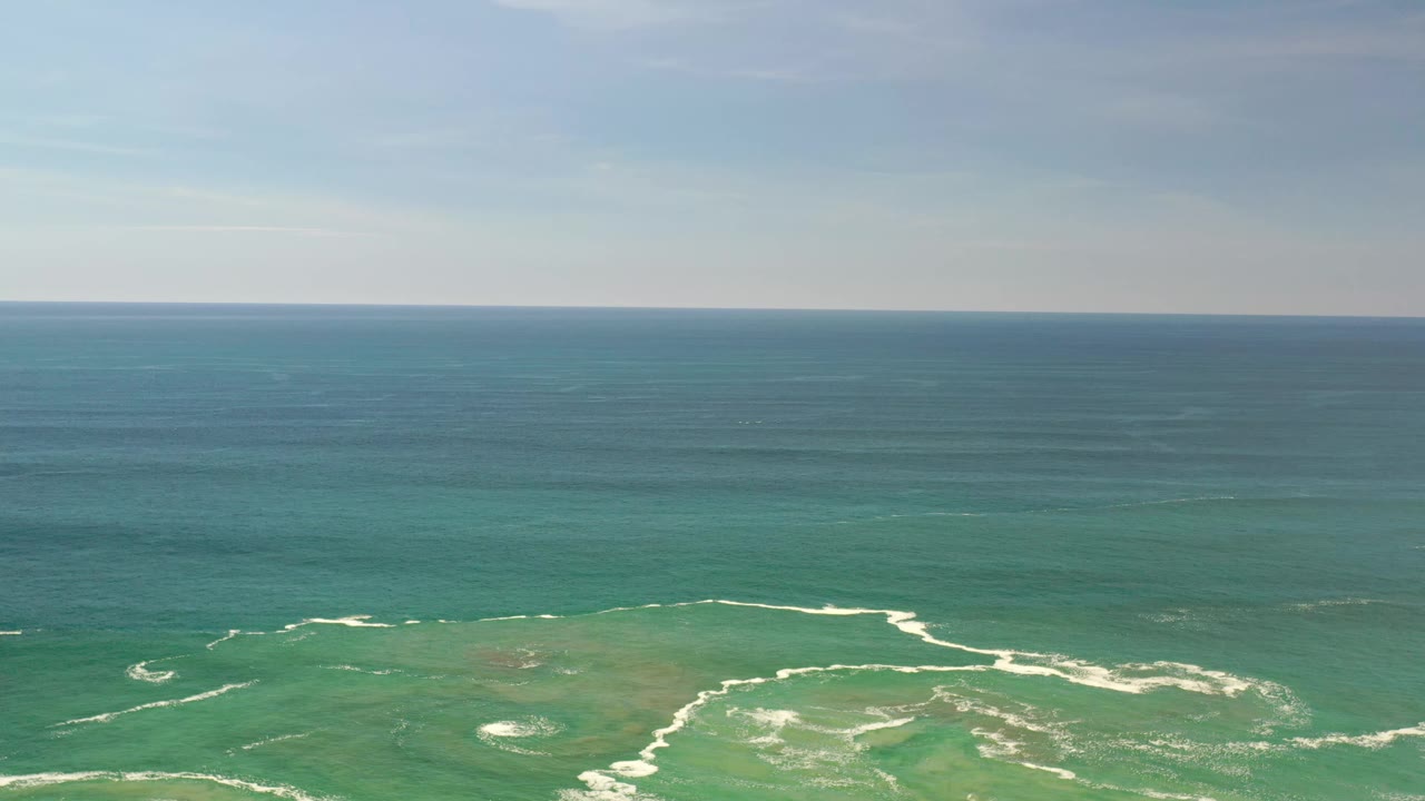 At 0:01, the Los Cabos sea holds a level horizon while pale breaking waves mark the shallow green water in the foreground, with no visible people.