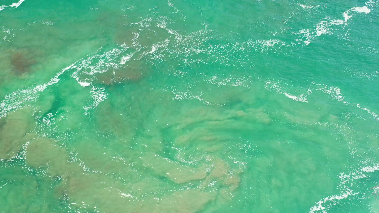 Overhead turquoise ocean water with foam and sandy shallows.
