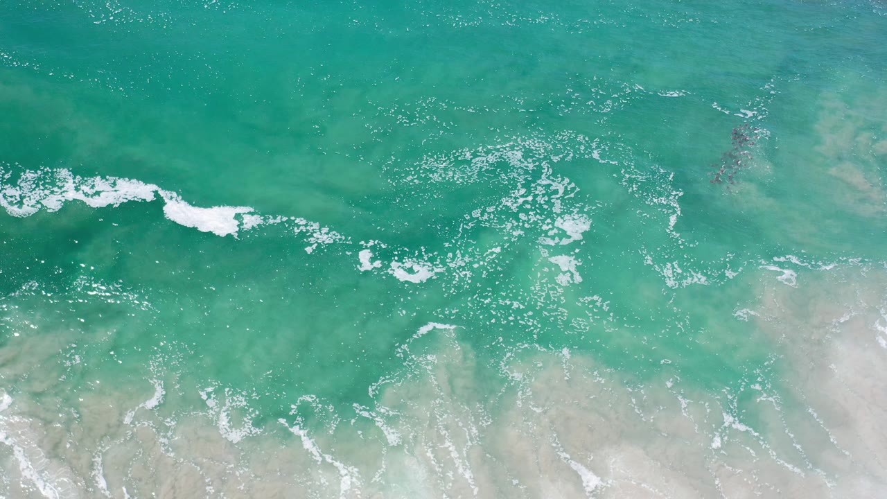 Overhead ocean surface with a thin white wave line and shallow sand below.