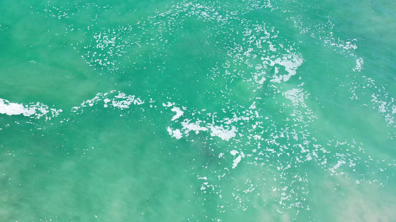 Sunlit turquoise water with clustered white foam near center right.