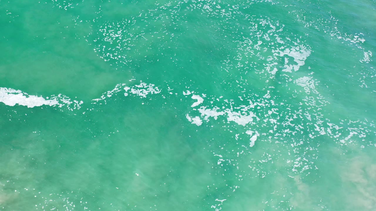 Foam patches and sunlit ripples over shallow beach water.