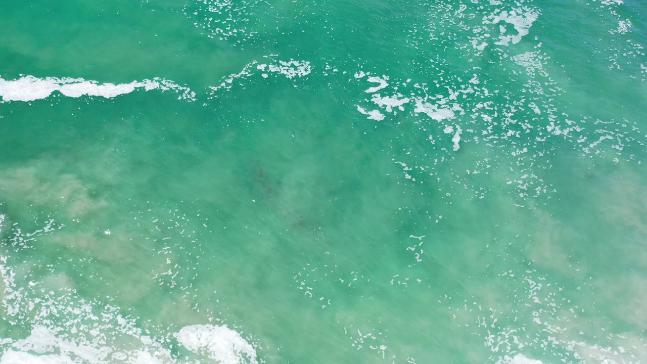 Overhead view of turquoise ocean water in Los Cabos, Mexico, with scattered white foam near the top and lower edge and no visible people.