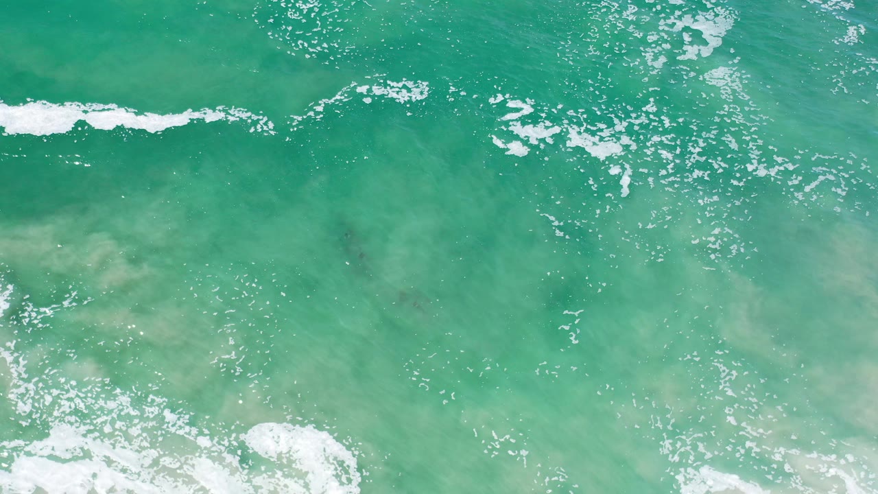 Sparkling turquoise sea with foam patches over shallow sand.