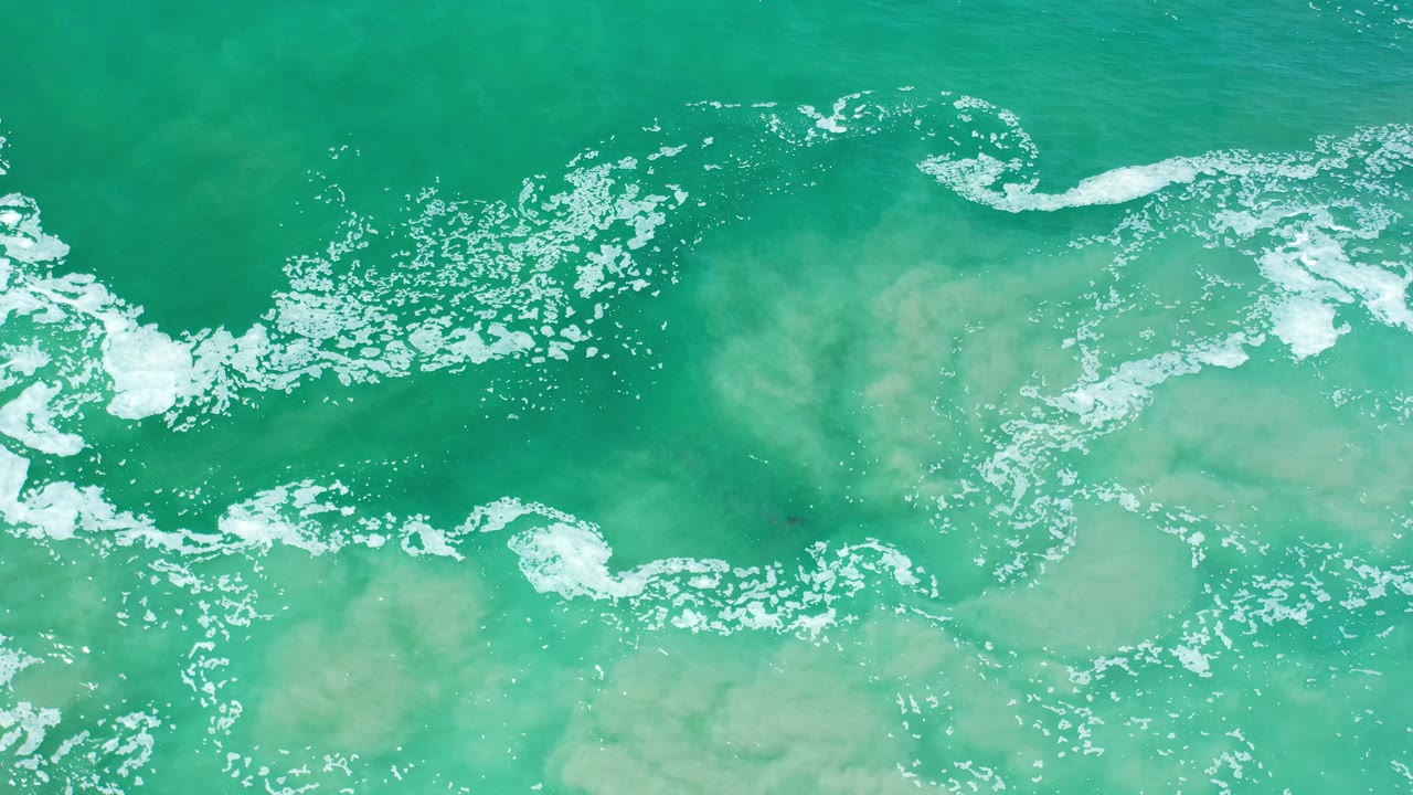 Aqua green surf in Los Cabos, Mexico fills the frame, with a brighter band of white foam curling across the upper center and no visible people.