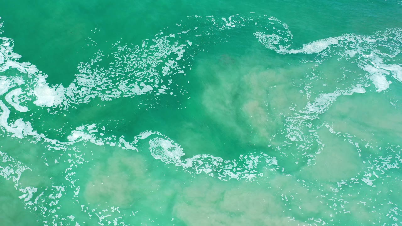 Clear ocean water with pale sand visible below and foam at top.