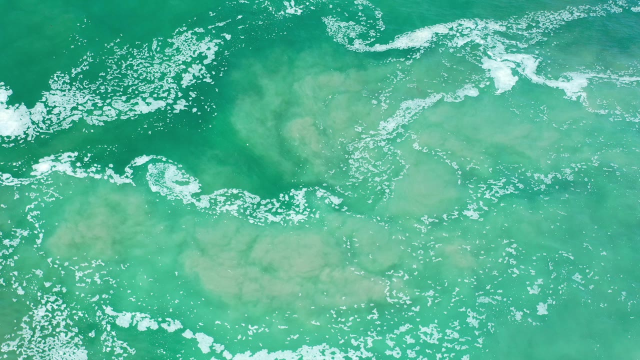 Turquoise water with a curved white foam line and sand below.