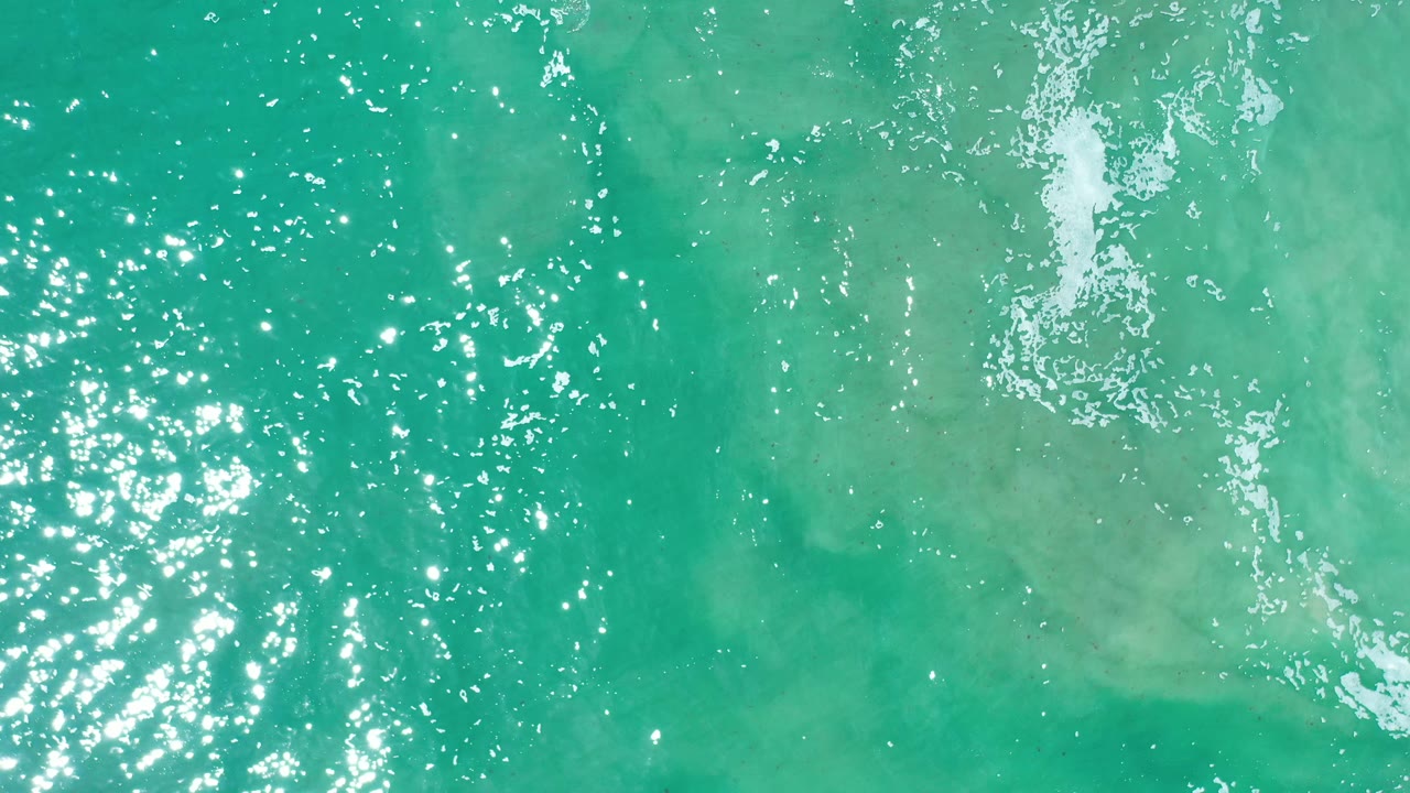 Aerial green water with scattered sparkle and pale froth.