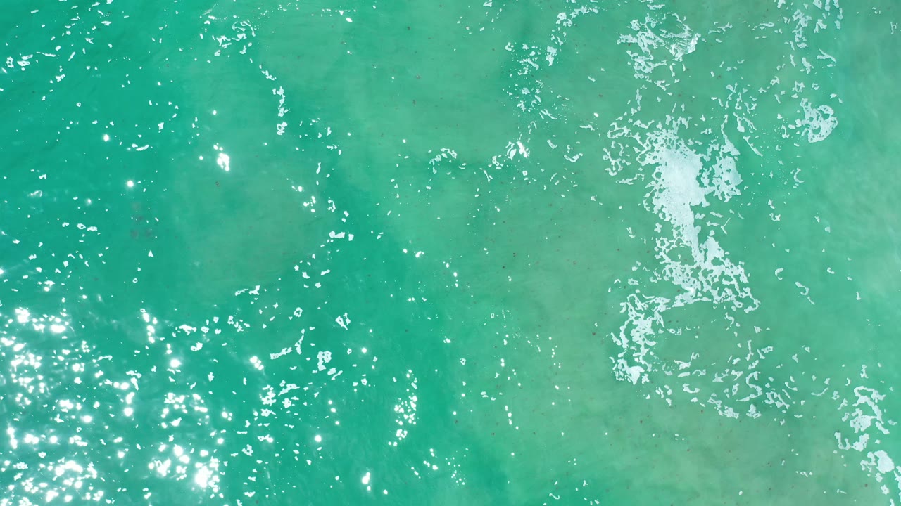 Overhead Los Cabos sea surface with blue-green water, small white foam streaks, and no visible people.