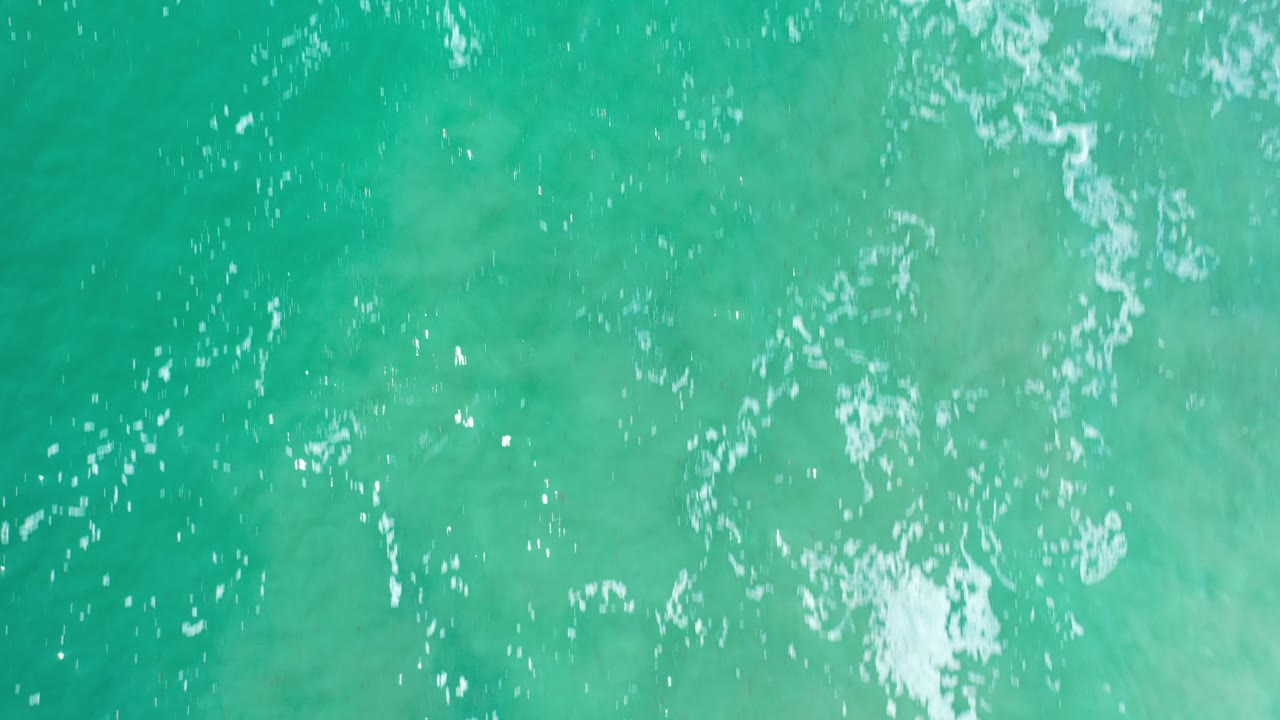 Overhead view of turquoise ocean water in Los Cabos, Mexico, with white foam crossing the upper part of the frame and no visible people.
