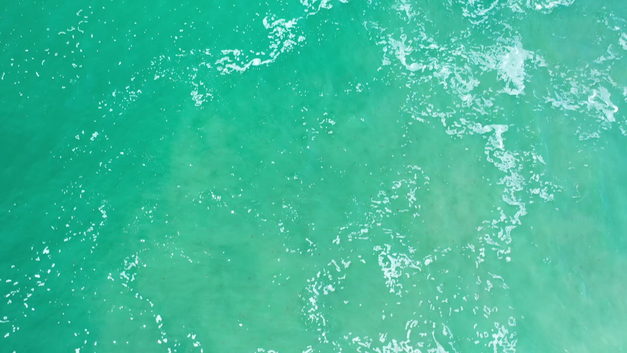 Top-down view of green ocean shallows in Los Cabos, Mexico, where small white crests break across the upper water surface with no visible people.