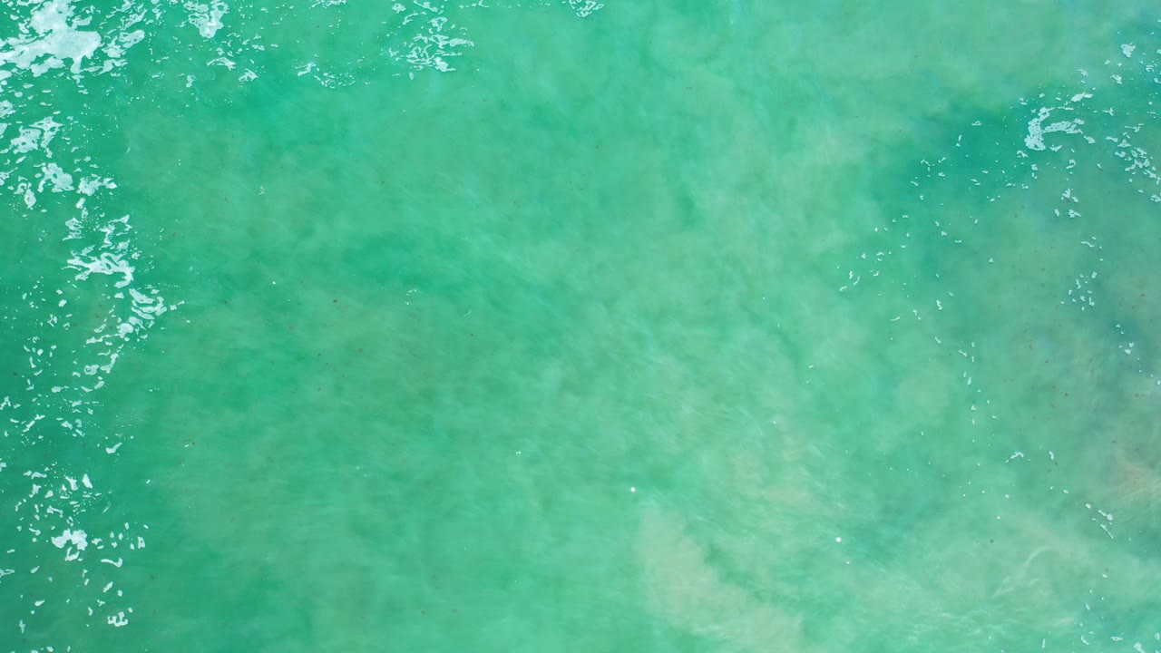 Turquoise water fills the frame with faint underwater shapes and thin foam marks.