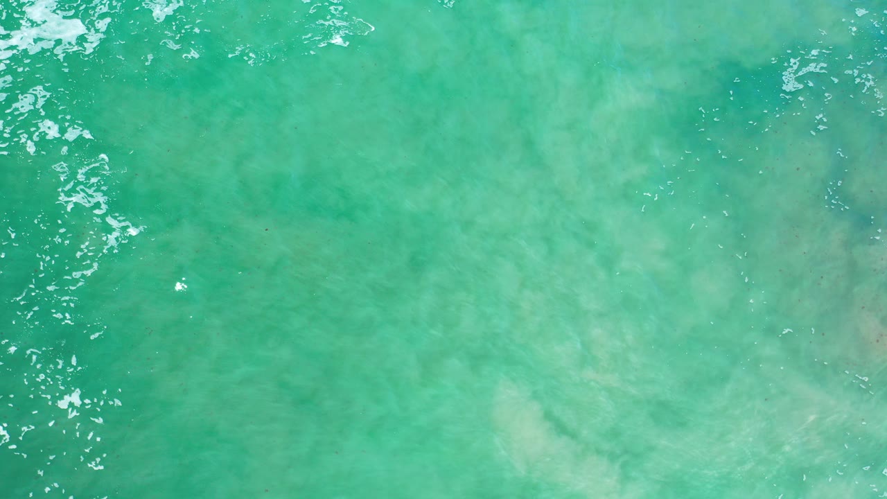 Turquoise ocean water with pale seabed and small white foam streaks.