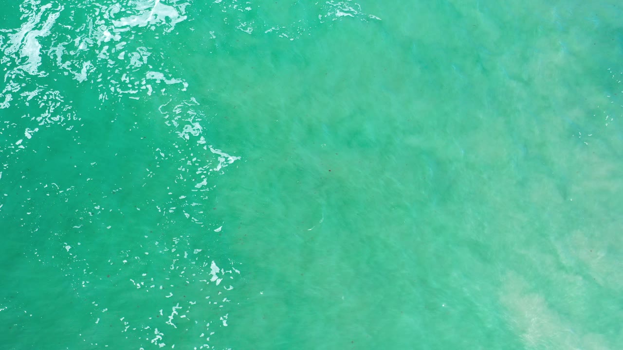 Overhead view of green-turquoise ocean water in Los Cabos, Mexico, with white surface ripples at the left and no visible people.