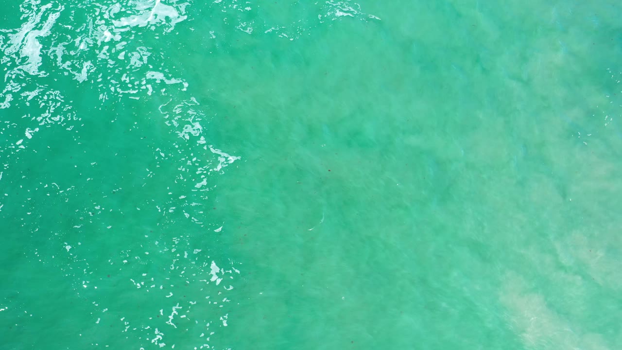 Top-down Los Cabos ocean frame showing turquoise water and a narrow area of white surf texture near the left-center, with no visible people.
