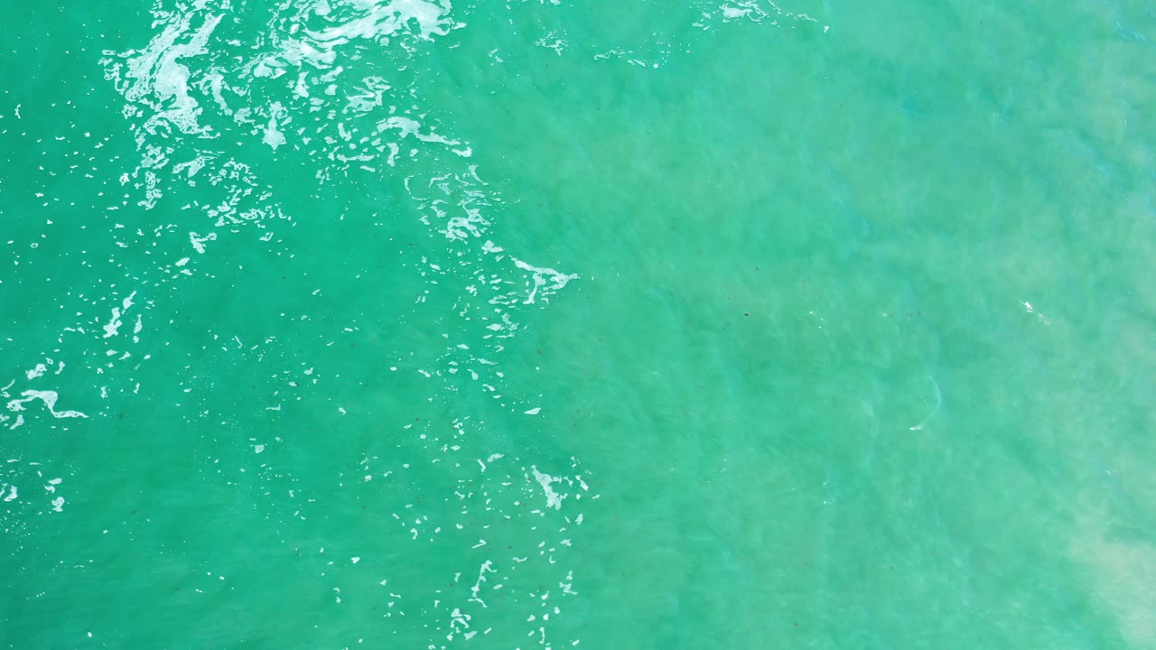 Turquoise ocean from above with bright wave flecks near the top edge.