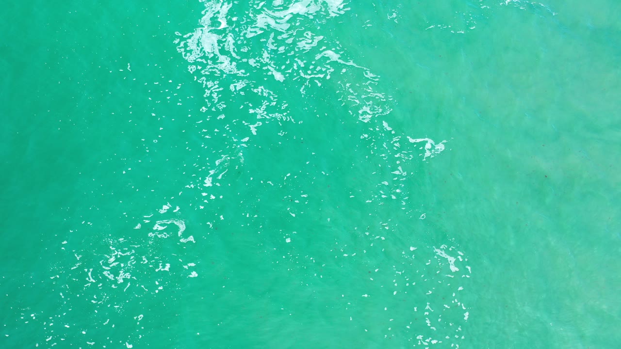Overhead view of turquoise water in Los Cabos, Mexico, with white sun glints near the upper left and no visible people.
