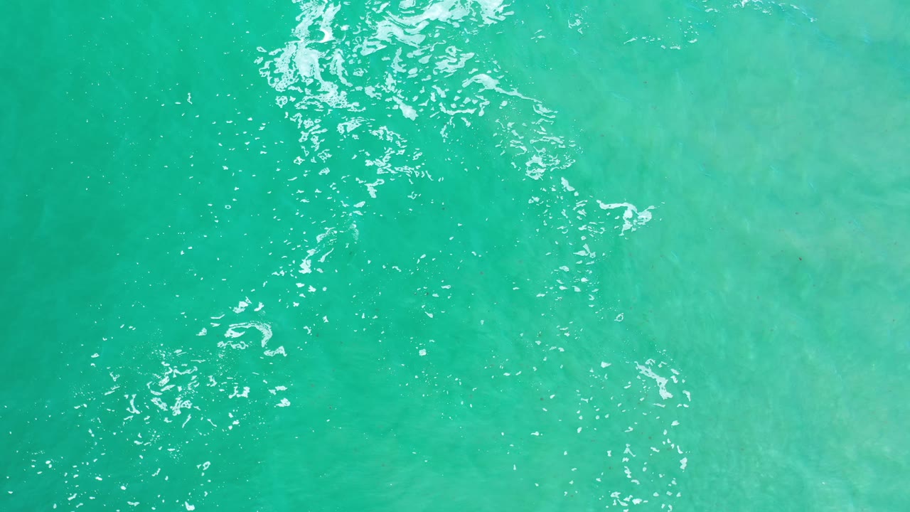Straight-down Los Cabos water view with small foam flecks through the center-left area and no visible people.