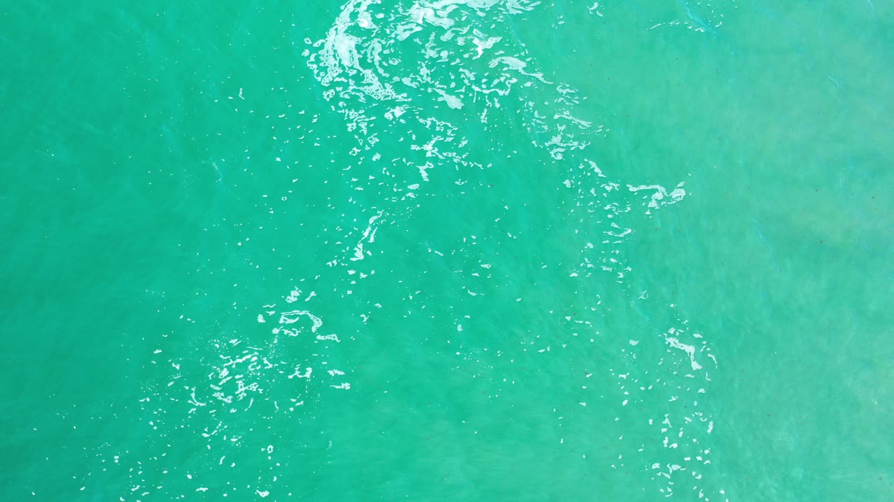 Top-down view of turquoise ocean water with white ripples.