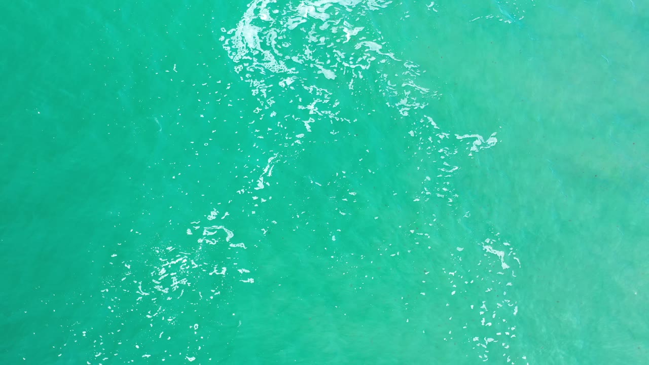 Clear aqua sea water in Los Cabos, Mexico, seen from above with scattered white highlights running near the left side and no visible people.