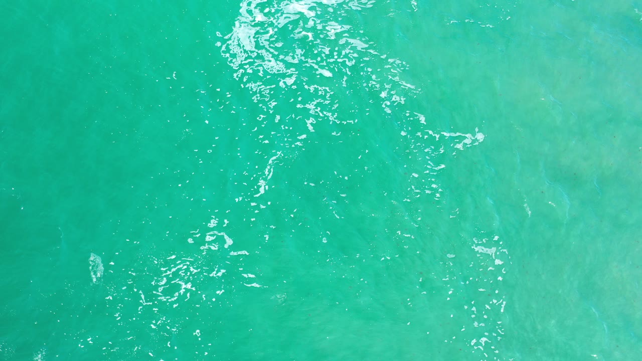 Overhead view of turquoise sea water in Los Cabos, Mexico, with bright white ripple highlights near the upper center and no visible people.