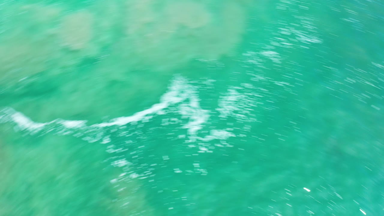 Overhead view of green sea in Los Cabos, Mexico, with white foam streaks crossing the upper half and no visible people.