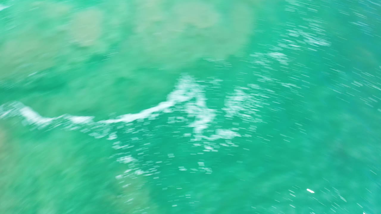 Aerial frame of green Los Cabos water with a curved white foam line moving across the center and no visible people.