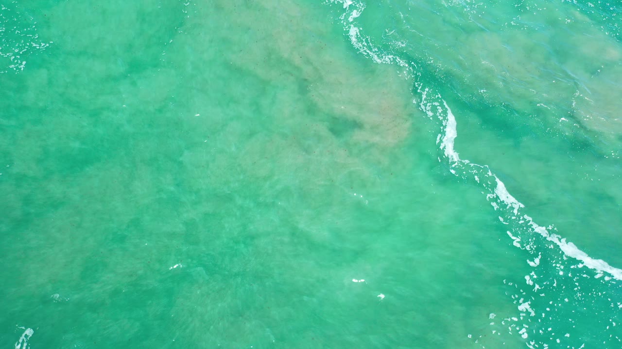 Green seawater with a diagonal streak of white foam over submerged rocks.