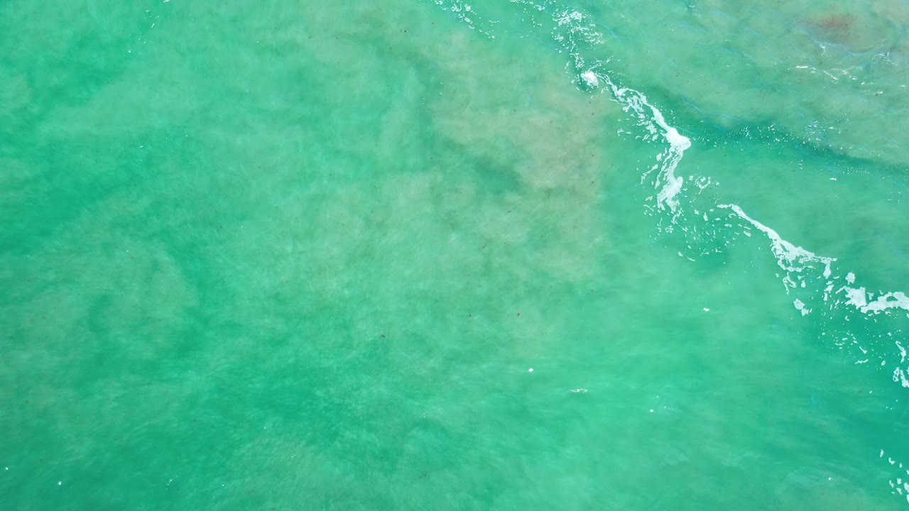 Overhead view of turquoise water over reef in Los Cabos, Mexico, with pale submerged patches near the top of frame and no visible people.