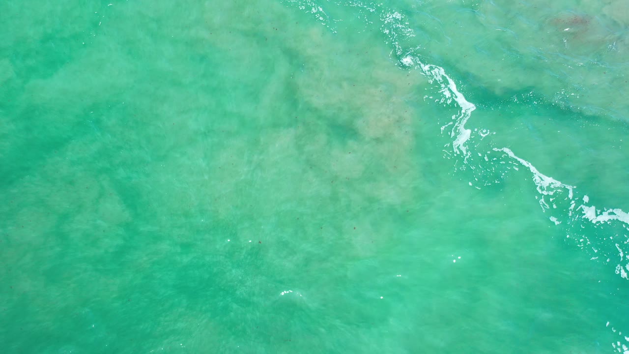 Turquoise ocean from above with reef shadows and broken white foam.