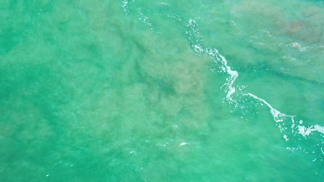 Turquoise water with scattered foam and reef shadows.
